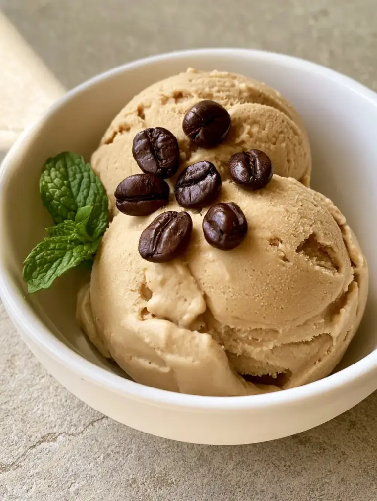 Close-up of light-tan Italian Coffee Gelato scoops with glossy coffee beans in a white bowl.