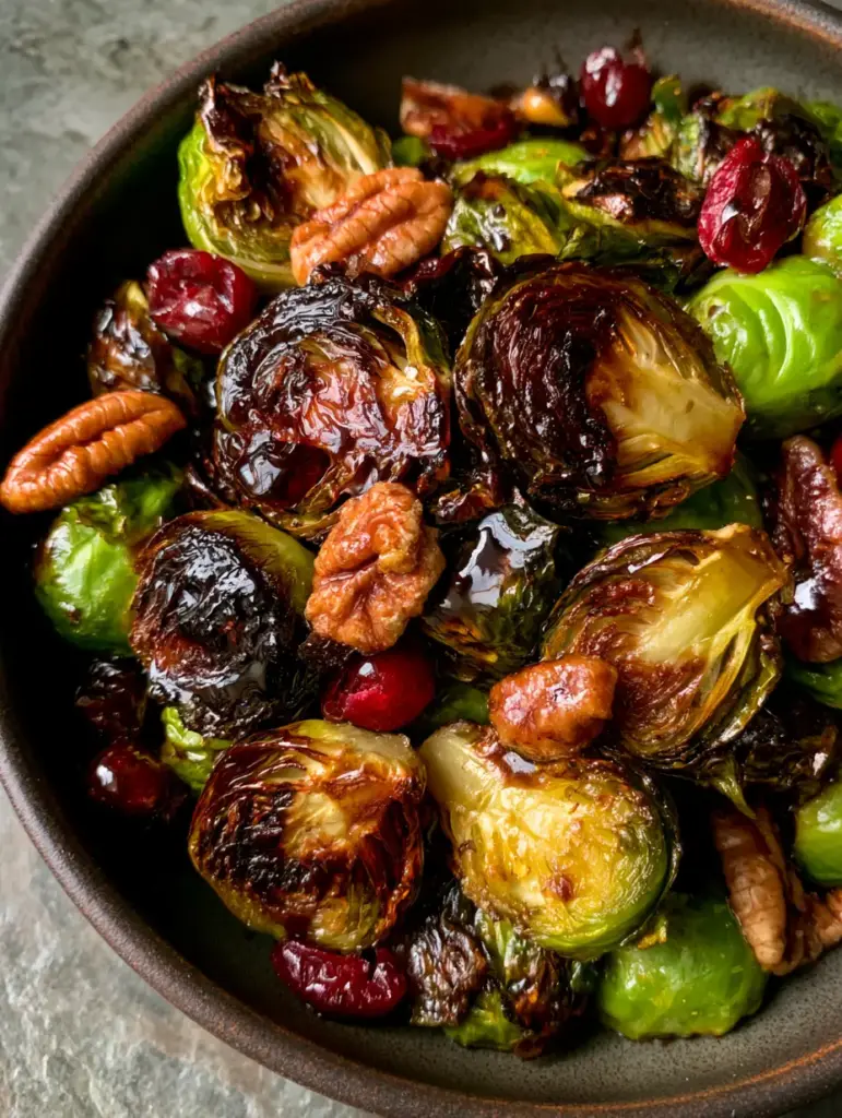 Roasted Brussels Sprouts with Balsamic Glaze, Pecans, and Cranberries 1 High angle photo of Roasted Brussels Sprouts drizzled with glossy balsamic glaze, pecans, and red cranberries.