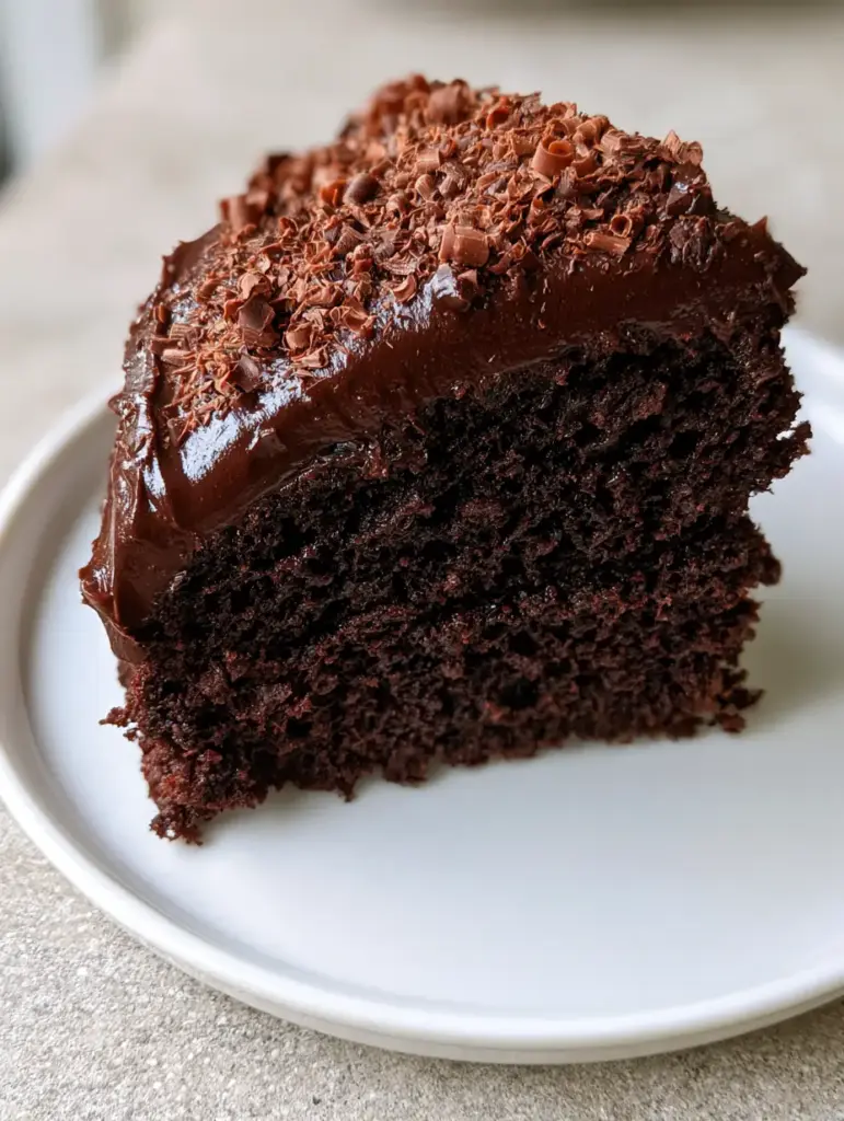 A single slice of deep dark chocolate sponge cake with visible aeration and glossy dark chocolate fudge frosting. (Midnight Chocolate Fudge Cake)