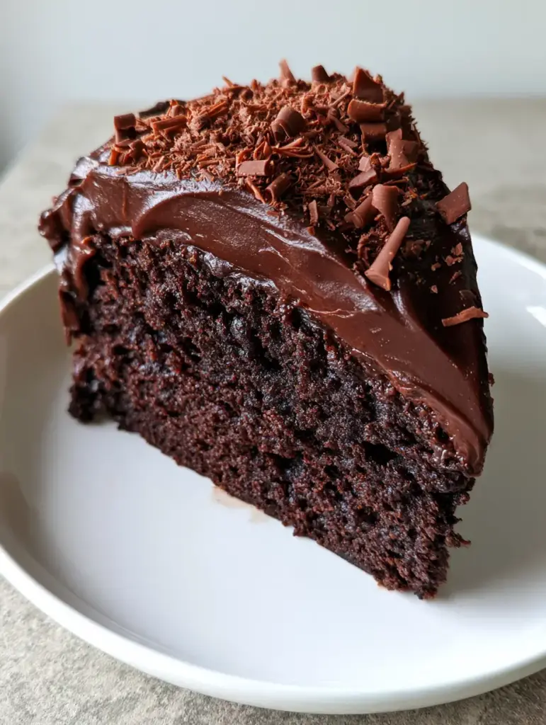 Midnight Chocolate Fudge Cake: The Ultimate Moist Dark Chocolate Sponge 1 High-angle shot of a slice of Midnight Chocolate Fudge Cake on a white ceramic plate, showing fine chocolate shavings.
