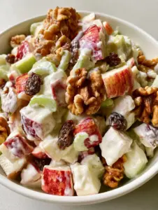 Close up of diced red and green apples coated in thick white dressing with visible walnuts. (Apple Salad Recipe)