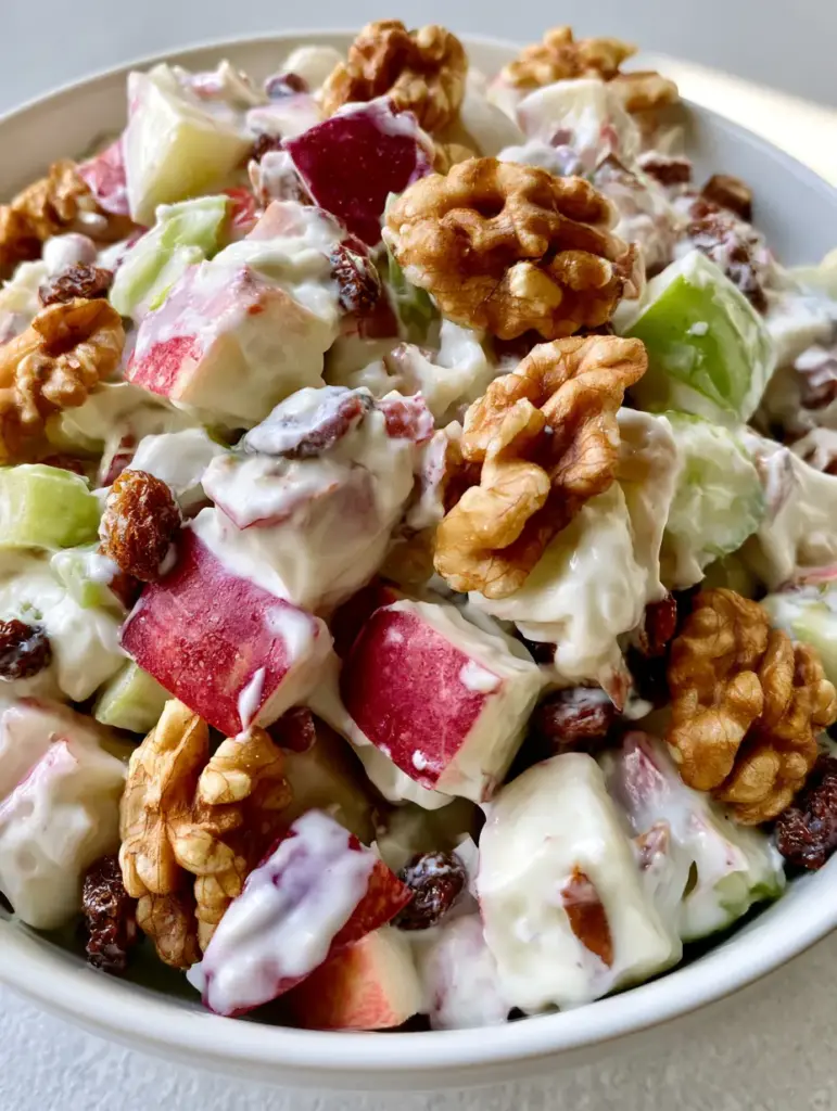 Apple Salad Recipe: The Ultimate Creamy Walnut and Celery Fruit Salad 1 Top-down view of a white ceramic bowl filled with creamy apple salad, celery, and dark raisins.